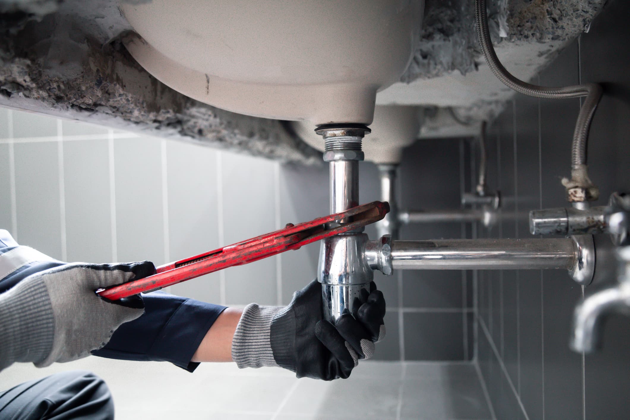 Licensed plumber repairing a leaking under-sink P-trap with a pipe wrench in McMinnville, Oregon